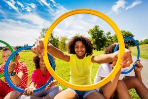 Group of kids with girl looking through colorful hoop in the park smiling and happy